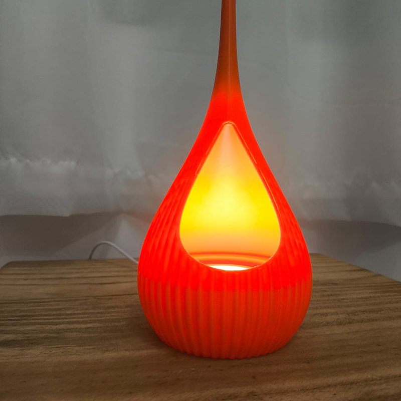 Peça de luz Gota de Orvalho vermelha acesa como uma chama, sobre mesa de madeira